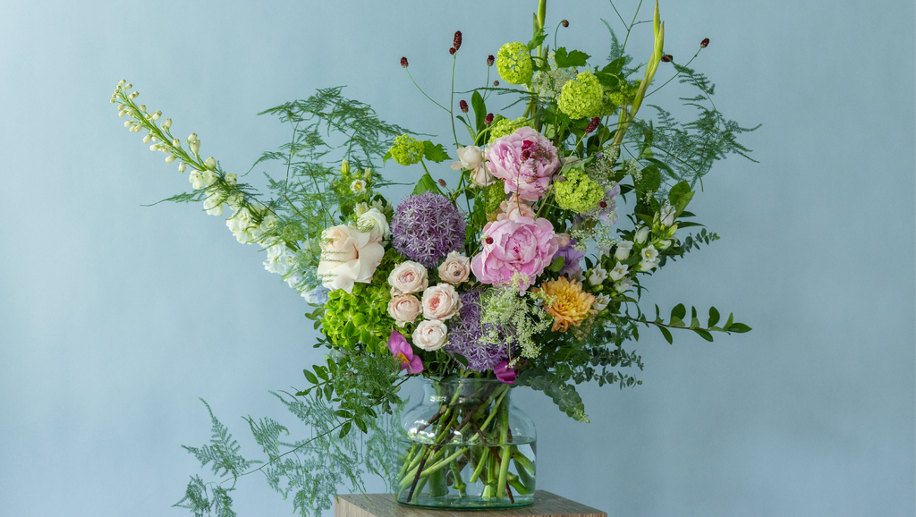 Garden-style summer arrangement by Charlotte Puxley Flowers featuring premium seasonal peonies, dancing textures, fresh green foliage, and soft pastel flowers.