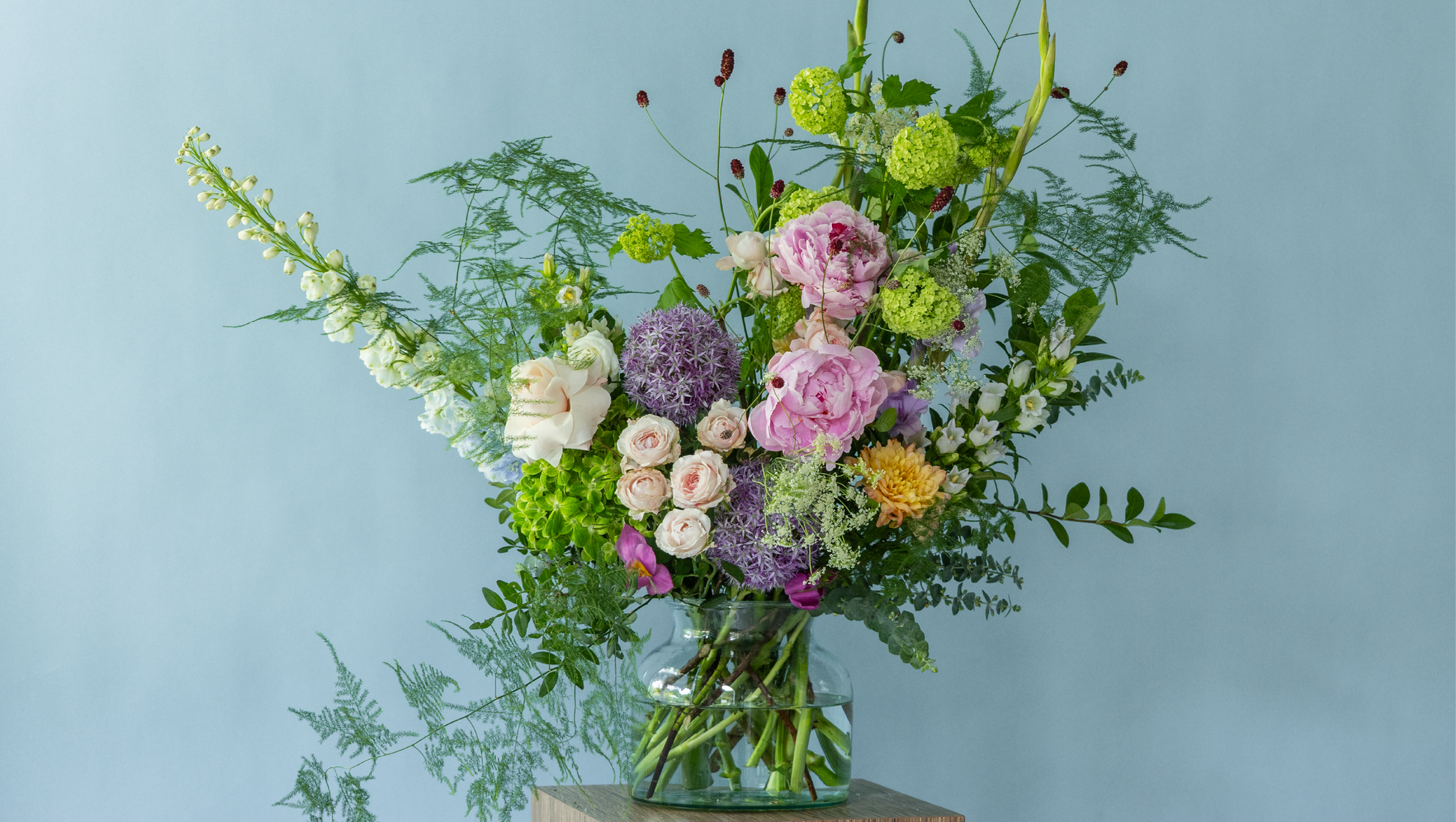 Garden-style summer arrangement by Charlotte Puxley Flowers featuring premium seasonal peonies, dancing textures, fresh green foliage, and soft pastel flowers.