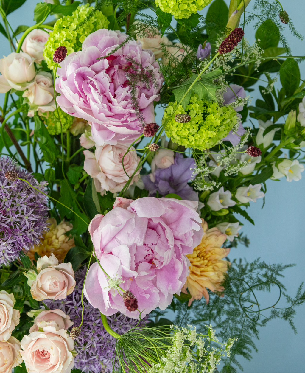 Garden-style summer arrangement by Charlotte Puxley Flowers featuring premium seasonal peonies, dancing textures, fresh green foliage, and soft pastel flowers.