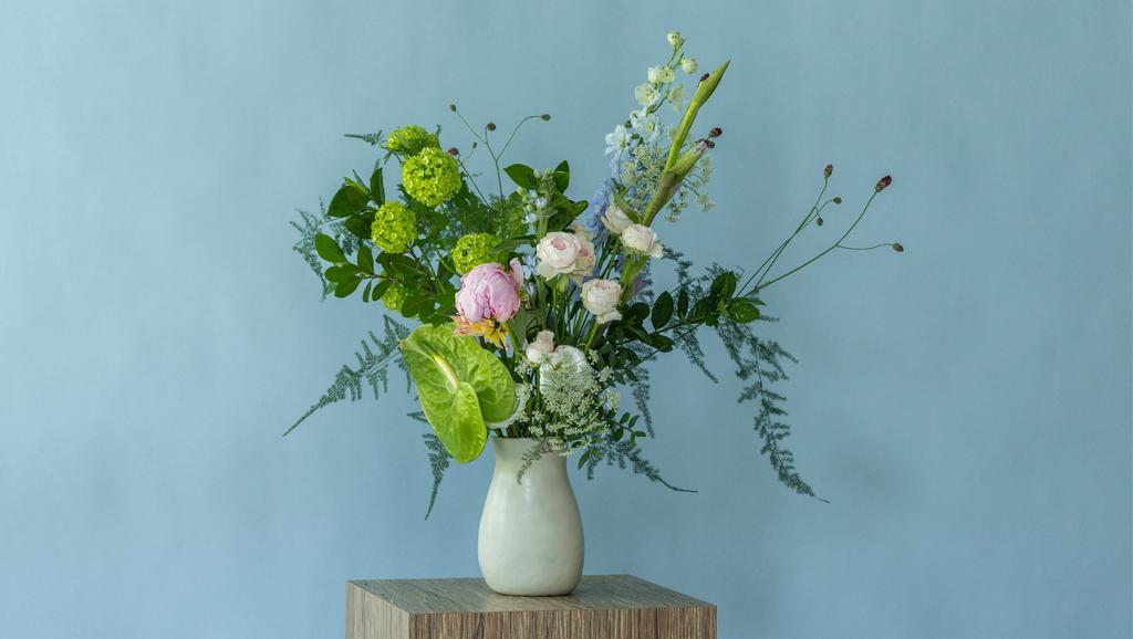 Elegant peony flower arrangement in a hand-crafted ceramic vase by Charlotte Puxley Flowers Singapore, showcasing seasonal pink peonies, spray roses, and lush summer greenery.